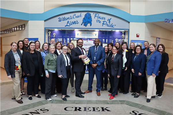 A group of men and women all dress in suit jackets and ties smile at the camera.